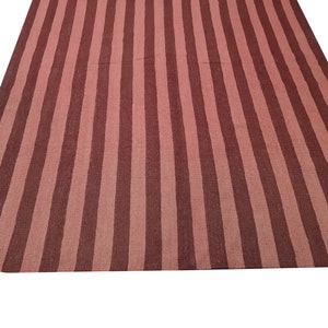 May include: A large, rectangular rug with a striped pattern. The rug features alternating vertical stripes of a muted reddish-brown and a lighter, dusty rose color. The rug is made of a woven material.