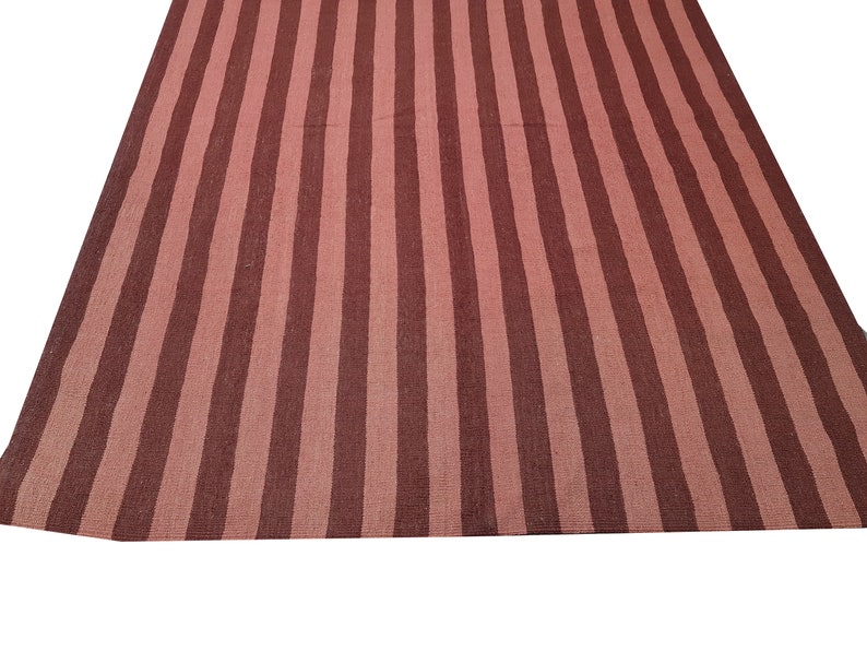May include: A large, rectangular rug with a striped pattern. The rug features alternating vertical stripes of a muted reddish-brown and a lighter, dusty rose color. The rug is made of a woven material.