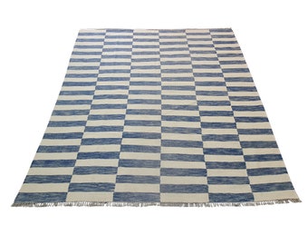 May include: A rectangular rug with a blue and white striped pattern. The rug has a checkerboard design with alternating blue and white horizontal stripes. The rug has a fringe along the bottom edge.