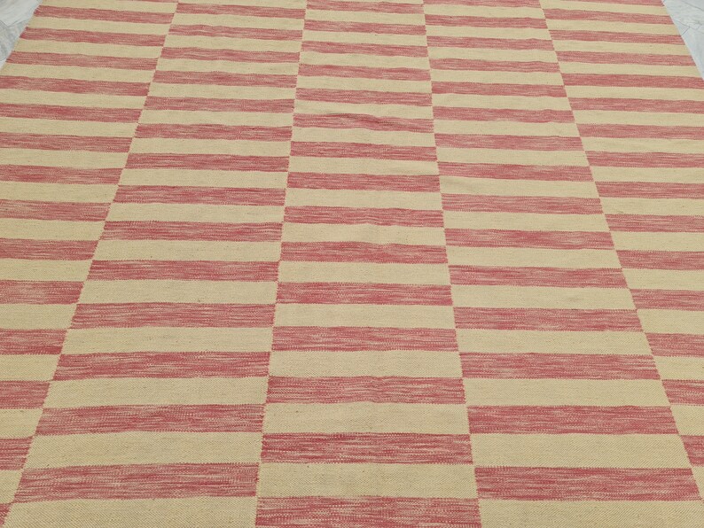 May include: A woven rug with a repeating pattern of alternating red and beige horizontal stripes. The stripes are evenly spaced and create a geometric design. The rug appears to be made of natural fibers.