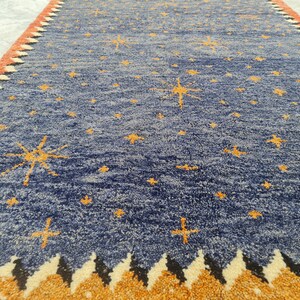 May include: A blue rug with a celestial design. The rug features a pattern of yellow stars scattered across the blue field. The border has a repeating pattern of orange, black, and white shapes.
