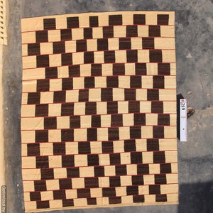 May include: A rectangular woven rug with a repeating pattern of alternating dark brown and beige squares. Thin red lines separate the horizontal rows. The rug is displayed on a gray surface.