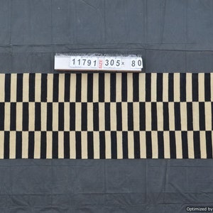 May include: A rectangular rug with a repeating pattern of black and beige vertical stripes. The rug measures approximately 120 inches long and 31.5 inches wide. The rug is made of a woven material and is displayed on a dark gray surface.