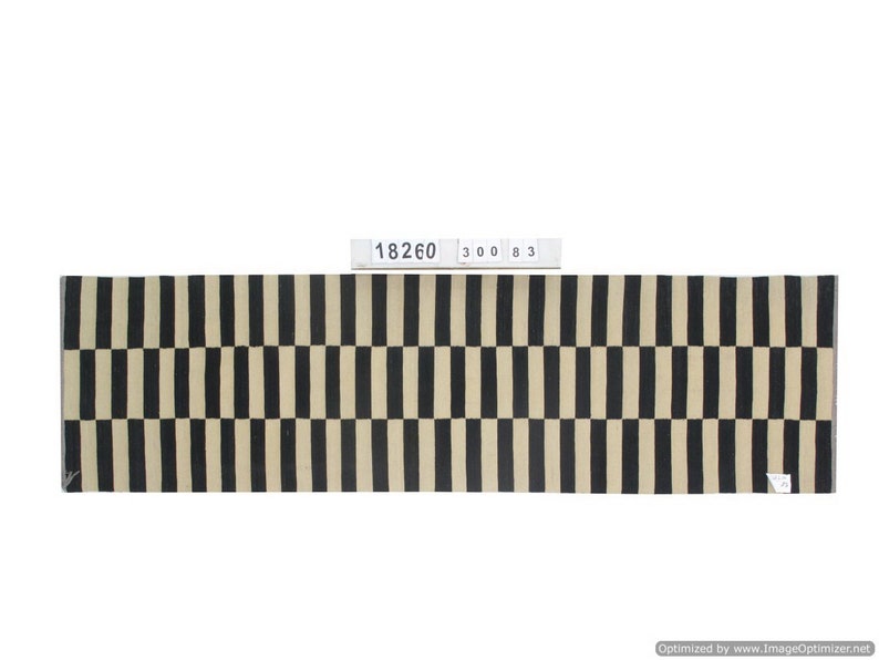 May include: A rectangular rug with a repeating pattern of black and beige vertical stripes. The rug has a woven texture and a label with the numbers "18260 300 83".