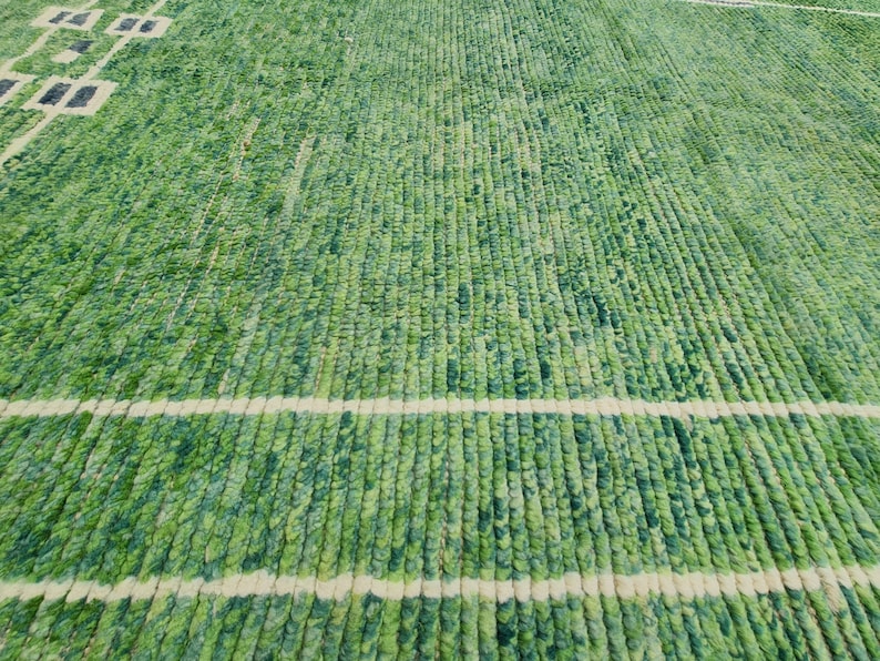Puede incluir: Alfombra verde y blanca con un dise&ntilde;o texturizado y tejido. La alfombra presenta un patr&oacute;n de l&iacute;neas verticales en varios tonos de verde, con rayas horizontales blancas y formas geom&eacute;tricas.