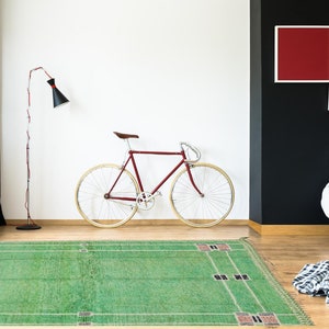 May include: A room with a green rug, a burgundy bicycle, and a black and white striped bedspread. A black floor lamp with a red cord stands near the bicycle. Red framed artwork hangs on a black wall.