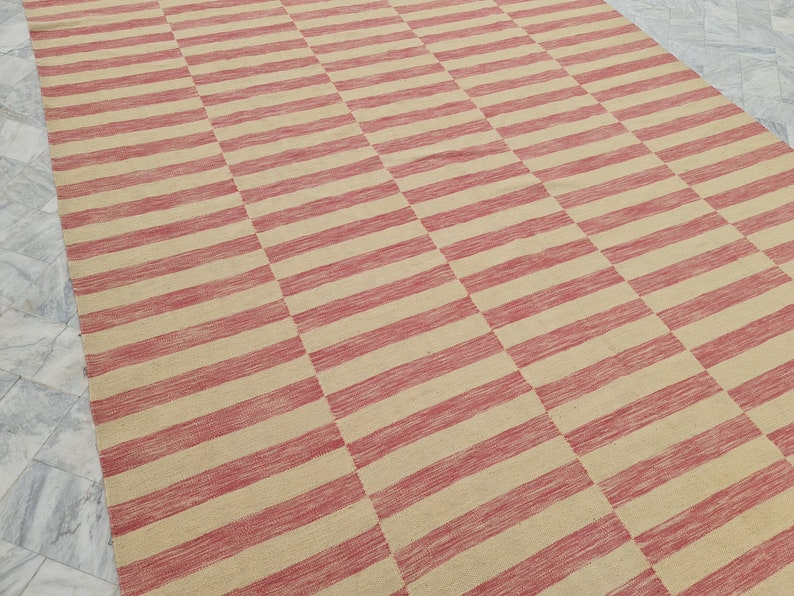 May include: A large rectangular rug with a repeating pattern of alternating red and beige horizontal stripes. The rug is made of a woven material and has a textured appearance. The stripes are evenly spaced and create a geometric design.