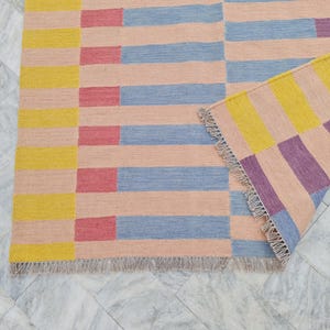 May include: A colorful area rug with a geometric pattern. The rug features horizontal stripes in peach, blue, red, and yellow. The rug's edge has a fringe.