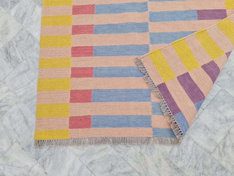 May include: A colorful area rug with a geometric pattern. The rug features horizontal stripes in peach, blue, red, and yellow. The rug's edge has a fringe.