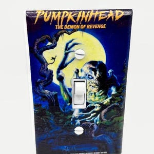 May include: A decorative light switch cover featuring the movie title "PUMPKINHEAD" and the tagline "THE DEMON OF REVENGE." The artwork depicts a monster with a full moon backdrop, with a white switch and screws.