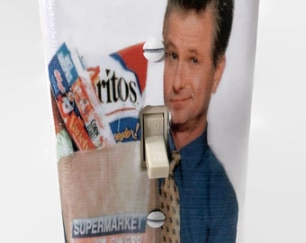 May include: A decorative light switch cover featuring a man in a blue shirt and tie, with a grocery bag filled with snacks. The switch is in the "NO" position. The words "SUPERMARKET SWEEP" are visible.