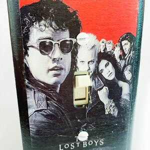 May include: A black light switch cover featuring the movie poster for "The Lost Boys." The poster art includes images of the film's characters, with the text "Sleep all day. Party all night. Never grow old. Never die. It's fun to be a vampire."
