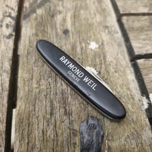 Può includere: Coltellino tascabile nero con lama argentata e le parole "Raymond Weil Geneve" stampate sul manico.