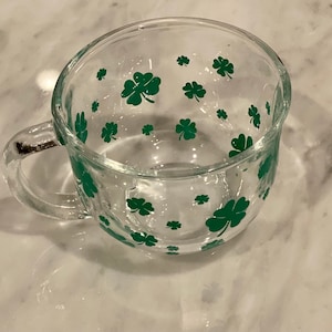 May include: A clear glass mug with a handle, featuring a green shamrock pattern.
