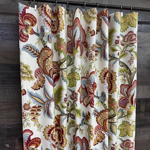 May include: A white shower curtain with a floral pattern in shades of red, blue, green, and yellow. The flowers are large and intricate, and the background is a light cream color.