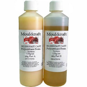 May include: Two plastic bottles of Mouldcraft SG2000 Fast Cast Polyurethane Resin. One bottle contains a light yellow liquid, the other a darker amber liquid. Each bottle has a white label with black text and a red, white, and blue logo. The kit is 120g.