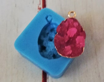 May include: A blue silicone mold for making resin jewelry, with a pink and gold resin pendant sitting next to it.