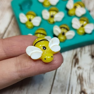 May include: A close-up of a yellow and black bee figurine with white wings. The bee is sitting on a finger.