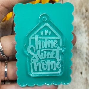 May include: Teal blue resin mould with a scalloped edge. The mould is shaped like a house with the words "Home Sweet Home" inside.