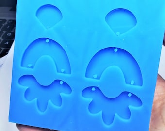 May include: Blue silicone mold with two sets of earring shapes. Each set includes a half-circle, a curved line, and a flower-shaped design.