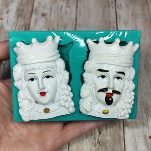May include: A pair of white silicone molds for making decorative figures. The molds are in a teal plastic tray. The molds are shaped like a king and queen with crowns and ornate details.
