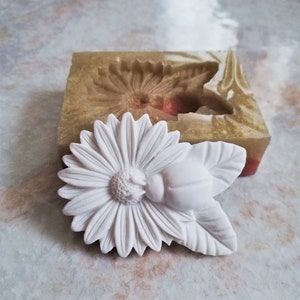 Könnte beinhalten: Weiße Silikonform zum Herstellen einer Gänseblümchen-Blume mit einem Käfer darauf. Die Form besteht aus flexiblem Silikon und hat ein detailliertes Design.