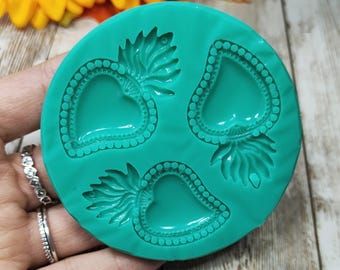 May include: A round, teal-colored silicone mold featuring three recessed cavities in the shape of sacred hearts. Each heart design includes a flame-like top and a beaded border detail, providing a clear impression for crafting projects.