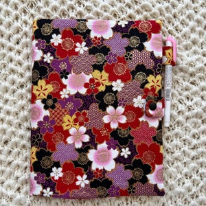 May include: A black binder with a floral pattern featuring pink, red, purple, and gold flowers. The binder has a snap closure and a pen holder.