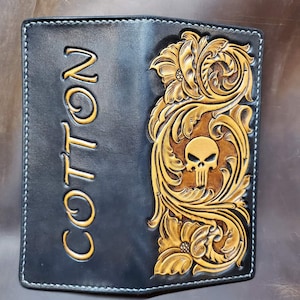 May include: Black leather wallet with a gold tooled design featuring a skull and floral patterns. The wallet is personalized with the name "COTTON" on the front.