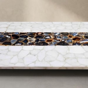 May include: A rectangular table top featuring a mosaic of white quartz pieces surrounding a central horizontal band composed of dark blue, black, and amber-toned agate slices. The surface is flat with a polished finish and a clean, straight edge.