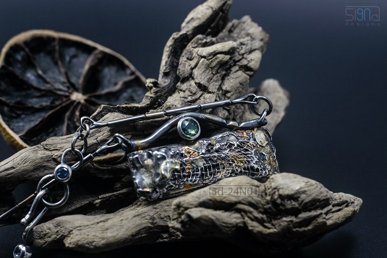 Mixed Metal Organic Necklace with Greenish Blue Sapphire and Topaz, Dark Texture, Statement Edgy Asymmetrical Chain, Silver and Gold Accents. On Dried Cactus Wood with Dried Lemon Behind.