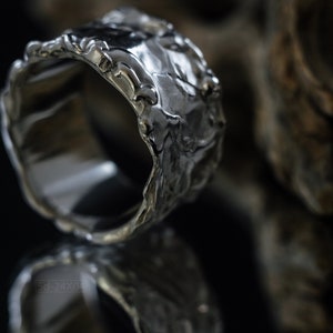 Molten Metal Chunky Ring, Dramatic Jewellery for Men and Women, Unisex Broad Ring with Irregular Edges. On Black Background with Mirror Reflection from Underneath and Dry Cactus Wood Behind.