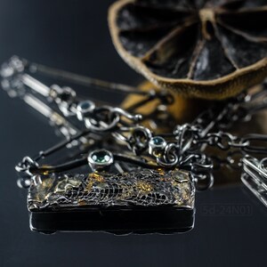Mixed Metal Organic Necklace with Greenish Blue Sapphire and Topaz, Dark Texture, Statement Edgy Asymmetrical Chain, Silver and Gold Accents. On Black Background with Reflection and a Dried Lemon Behind.