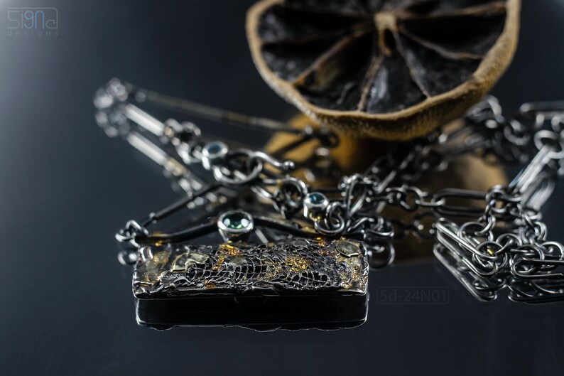 Mixed Metal Organic Necklace with Greenish Blue Sapphire and Topaz, Dark Texture, Statement Edgy Asymmetrical Chain, Silver and Gold Accents. On Black Background with Reflection and a Dried Lemon Behind.