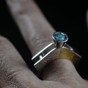 Contemporary ring with reticulated sterling silver and keum boo 24k gold foil and blue topaz stone, double-sided. On Finger.