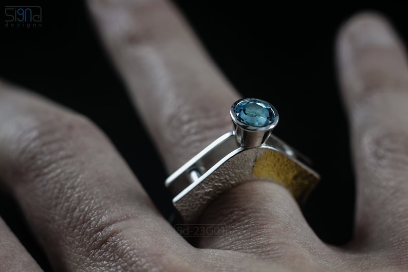 Contemporary ring with reticulated sterling silver and keum boo 24k gold foil and blue topaz stone, double-sided. On Finger.