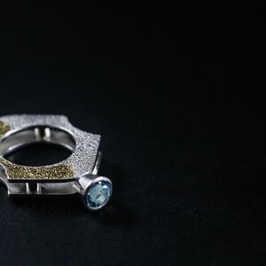 Contemporary ring with reticulated sterling silver and keum boo 24k gold foil and blue topaz stone, double-sided. On Black Background.