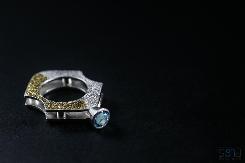 Contemporary ring with reticulated sterling silver and keum boo 24k gold foil and blue topaz stone, double-sided. On Black Background.