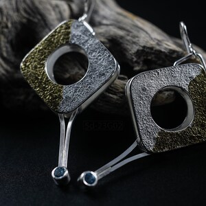 Contemporary dangle earrings with reticulated sterling silver, keum boo 24k gold foil and blue topaz, double-sided. On Dry Cactus Wood.