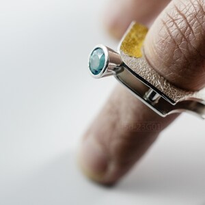 Contemporary ring with reticulated sterling silver and keum boo 24k gold foil and blue topaz stone, double-sided. On Finger.