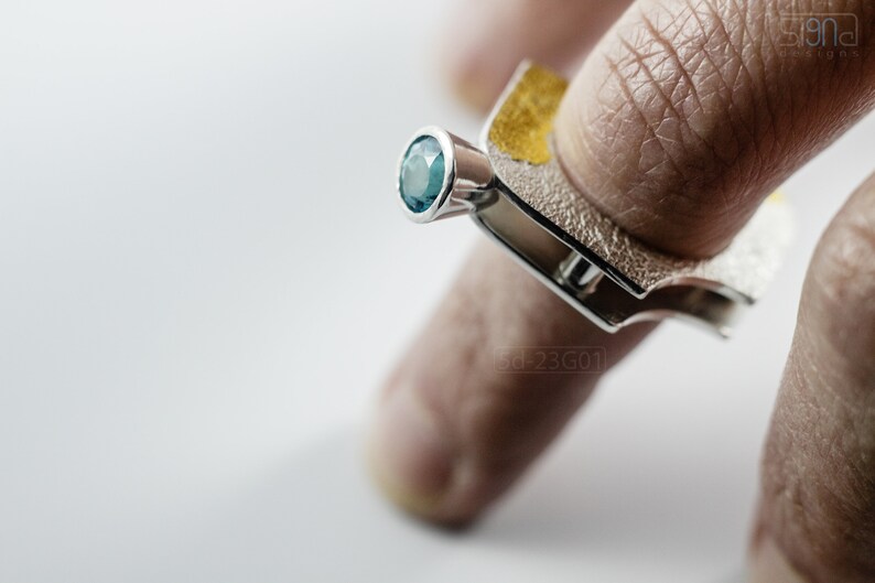 Contemporary ring with reticulated sterling silver and keum boo 24k gold foil and blue topaz stone, double-sided. On Finger.