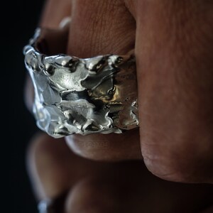 Molten Metal Chunky Ring, Dramatic Jewellery for Men and Women, Unisex Broad Ring with Irregular Edges. On Black Background with Mirror Reflection from Underneath. On Finger.