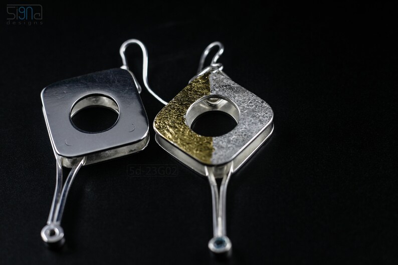 Contemporary dangle earrings with reticulated sterling silver, keum boo 24k gold foil and blue topaz, double-sided. On Black Background. One with the Front side UP and the Other with the Back Side Up.
