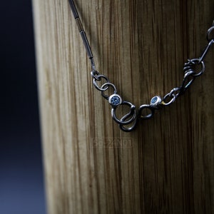 Mixed Metal Organic Necklace with Greenish Blue Sapphire and Topaz, Dark Texture, Statement Edgy Asymmetrical Chain, Silver and Gold Accents. Clasp Detail on Wood.