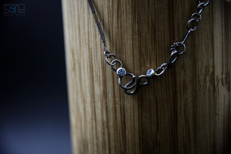 Mixed Metal Organic Necklace with Greenish Blue Sapphire and Topaz, Dark Texture, Statement Edgy Asymmetrical Chain, Silver and Gold Accents. Clasp Detail on Wood.