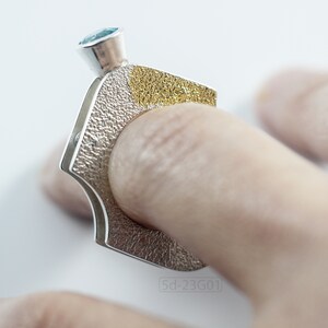 Contemporary ring with reticulated sterling silver and keum boo 24k gold foil and blue topaz stone, double-sided. On finger.
