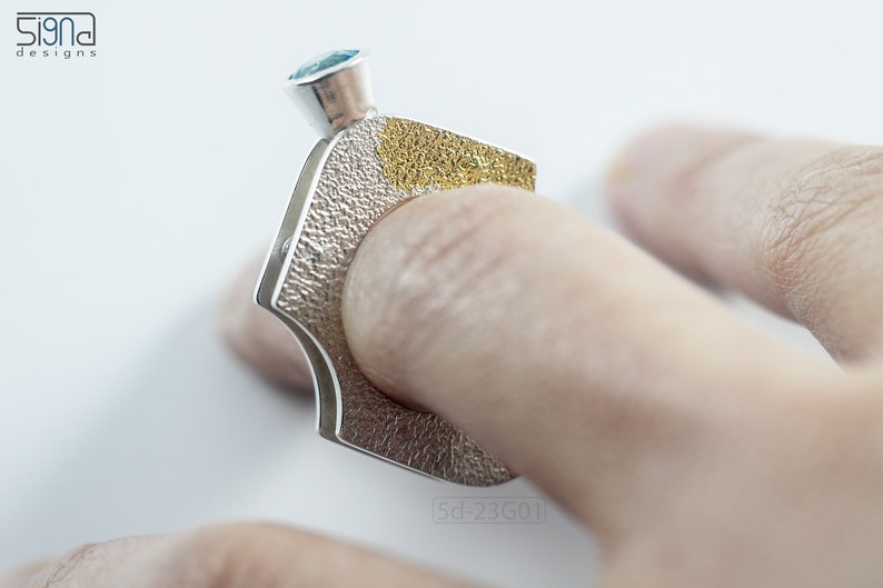 Contemporary ring with reticulated sterling silver and keum boo 24k gold foil and blue topaz stone, double-sided. On finger.