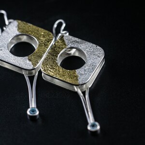Contemporary dangle earrings with reticulated sterling silver, keum boo 24k gold foil and blue topaz, double-sided. On Black Background.