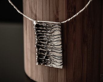 May include: A silver pendant necklace with a textured, wavy design. The pendant is hanging from a silver chain.