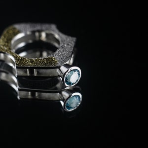 Contemporary ring with reticulated sterling silver and keum boo 24k gold foil and blue topaz stone, double-sided. On Mirror, Black Background.